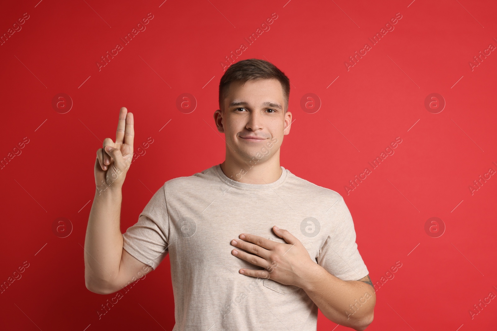 Photo of Man showing oath gesture on red background. Making promise