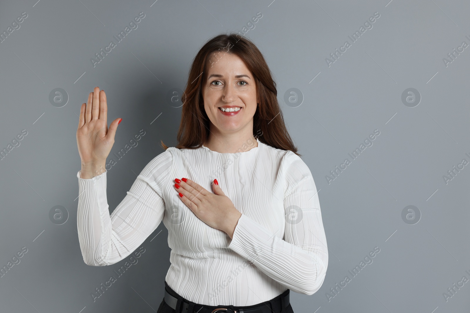 Photo of Woman making promise with raised hand on grey background. Oath gesture