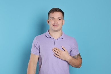 Man making promise on light blue background. Oath gesture