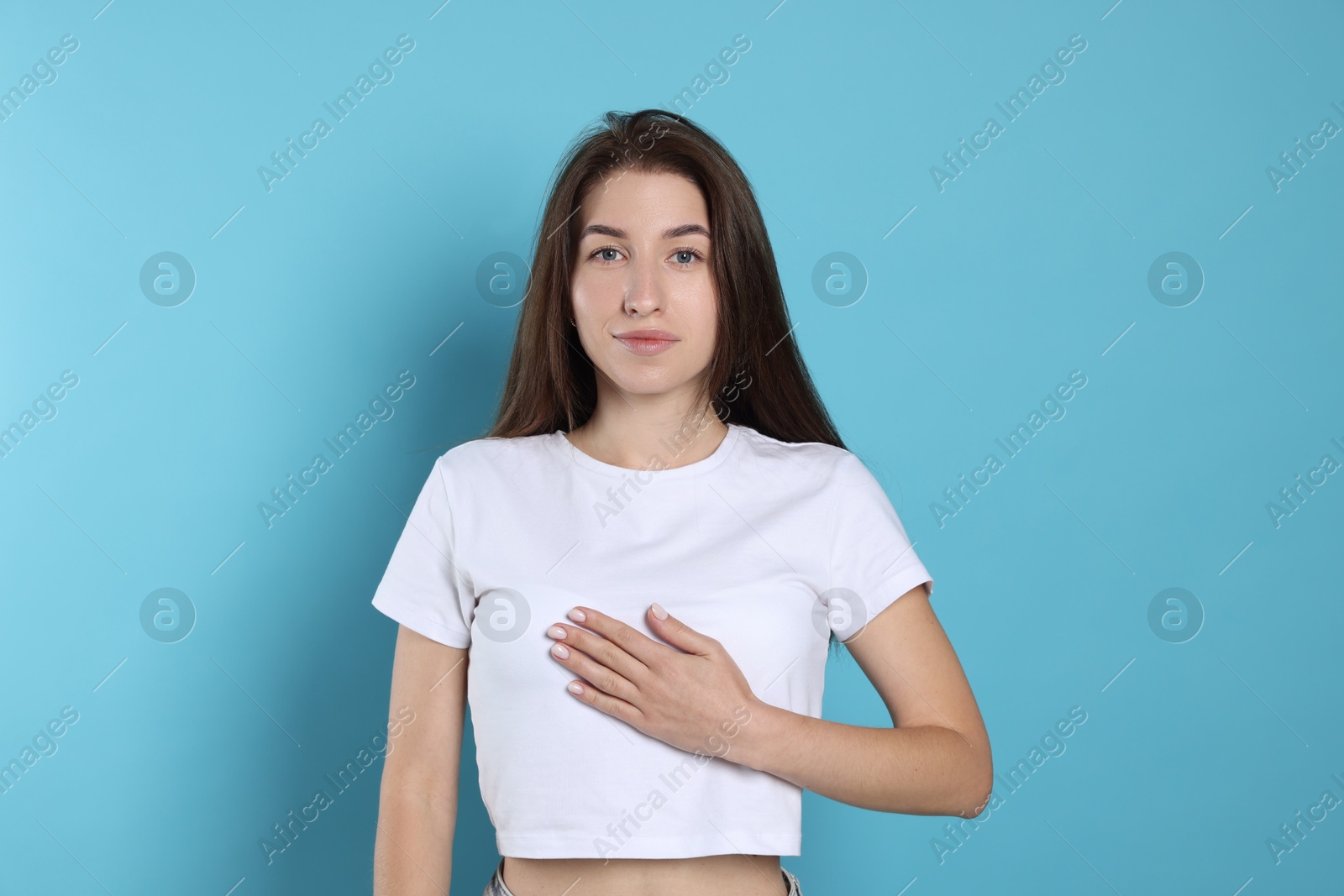 Photo of Woman making promise on light blue background. Oath gesture