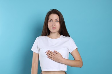 Woman making promise on light blue background. Oath gesture