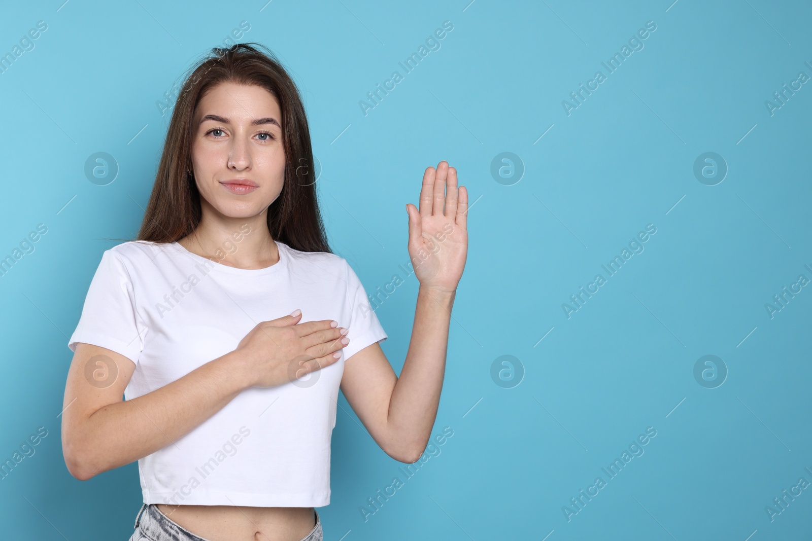 Photo of Woman making promise with raised hand on light blue background, space for text. Oath gesture