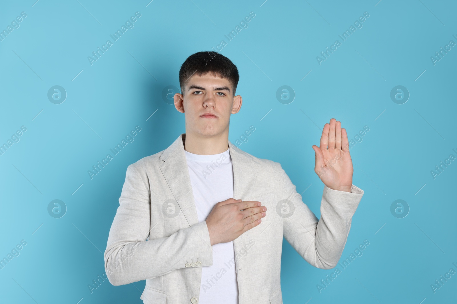 Photo of Man making promise with raised hand on light blue background. Oath gesture