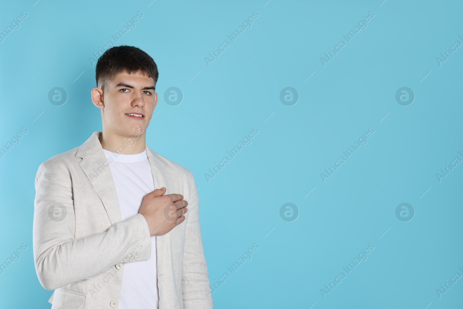 Photo of Man making promise on light blue background, space for text. Oath gesture