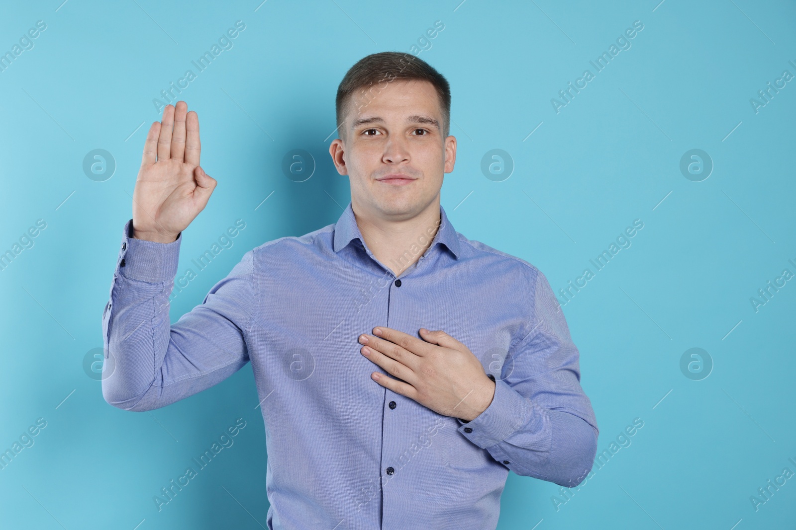 Photo of Man making promise with raised hand on light blue background. Oath gesture