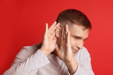 Photo of Man showing hand to ear gesture on red background