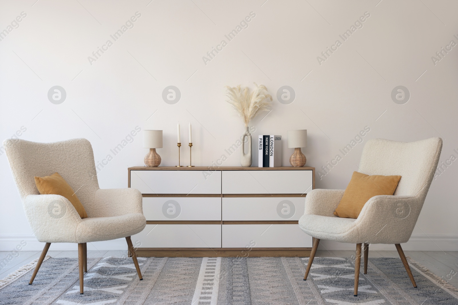 Photo of Soft armchairs and chest of drawers near white wall indoors