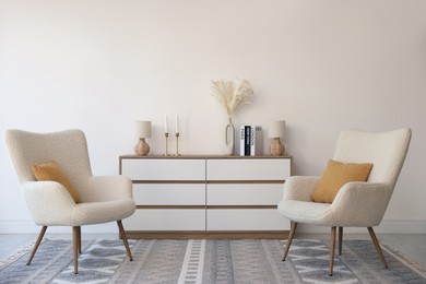 Soft armchairs and chest of drawers near white wall indoors