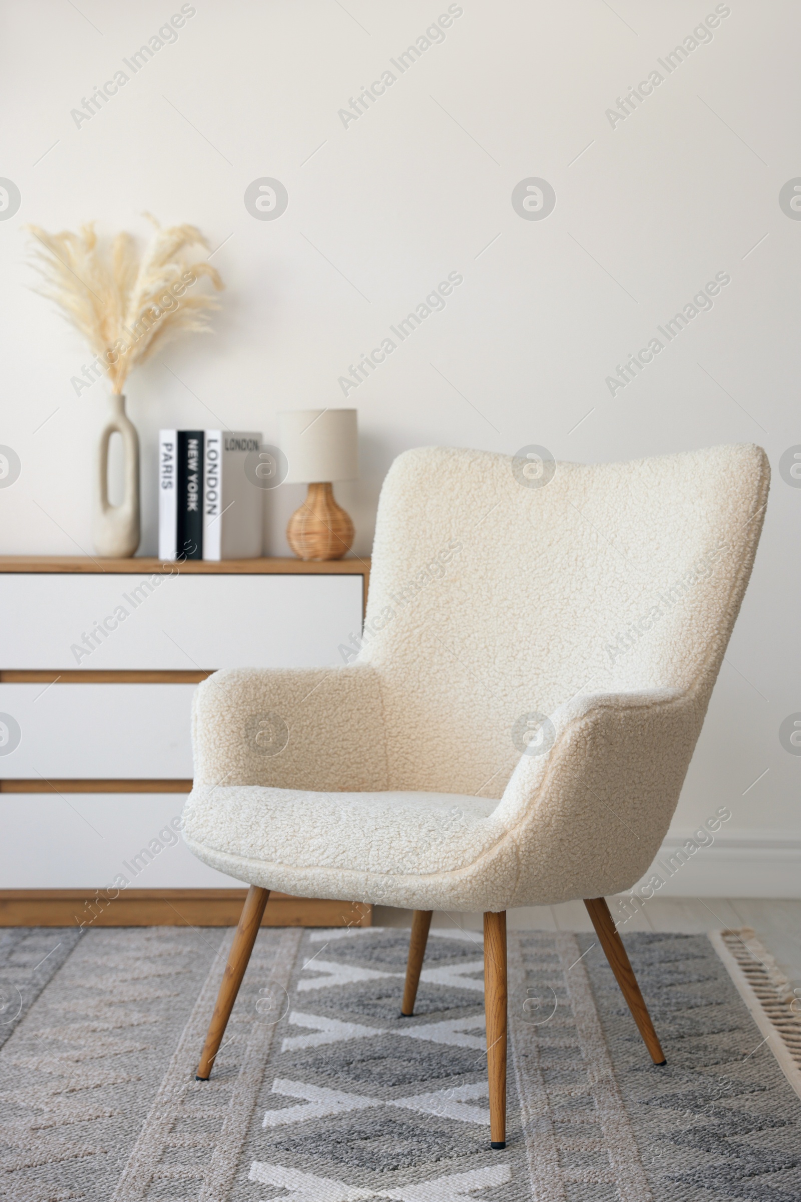 Photo of Soft armchair and chest of drawers near white wall indoors