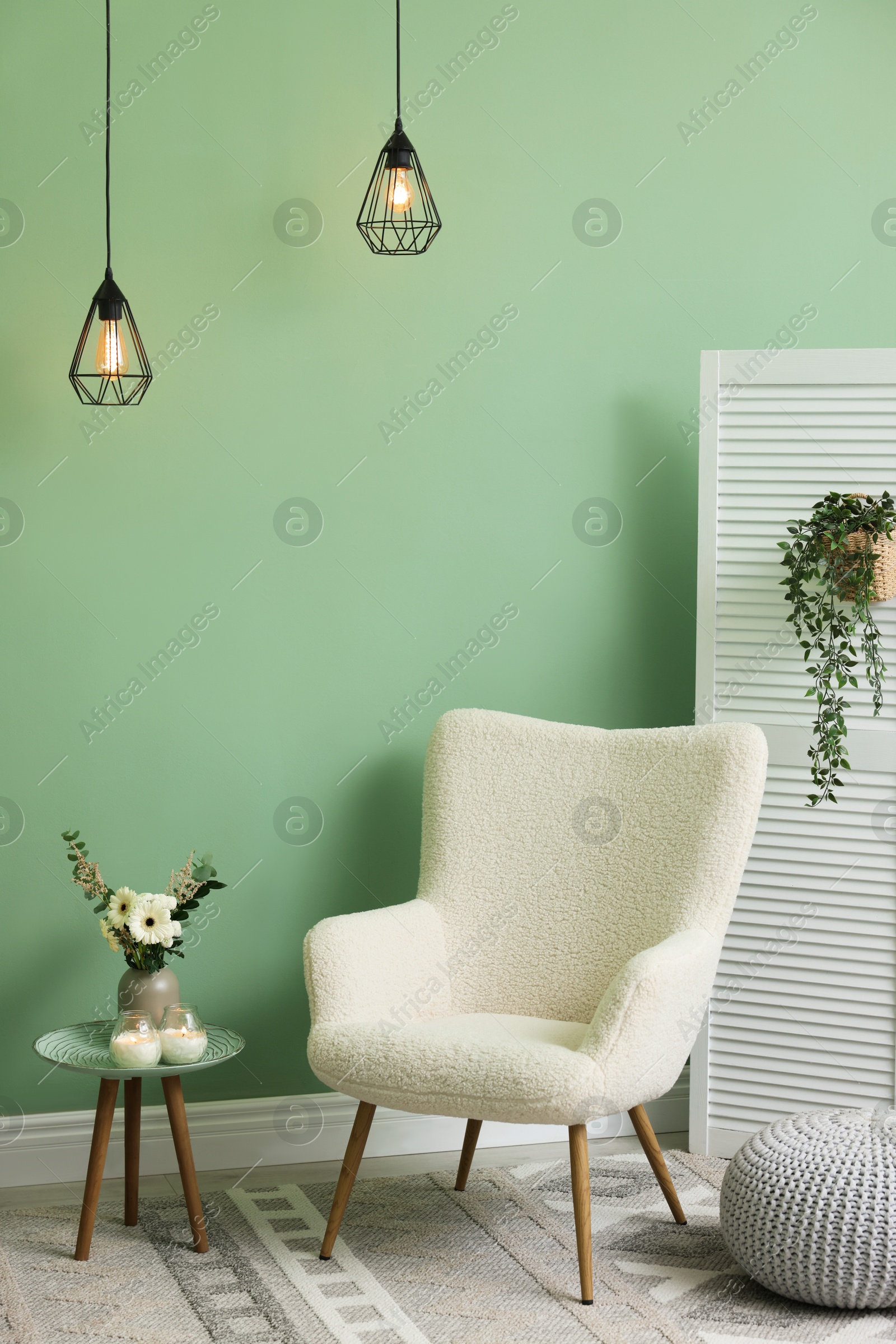 Photo of Soft armchair, side table, folding screen and floral decor in room