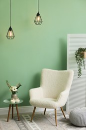 Photo of Soft armchair, side table, folding screen and floral decor in room