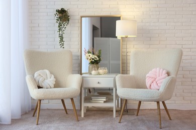 Soft armchairs, side table, mirror and floral decor in room