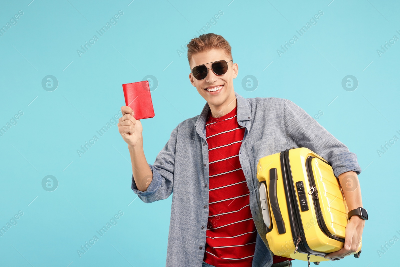 Photo of Happy traveller with suitcase and passport on light blue background