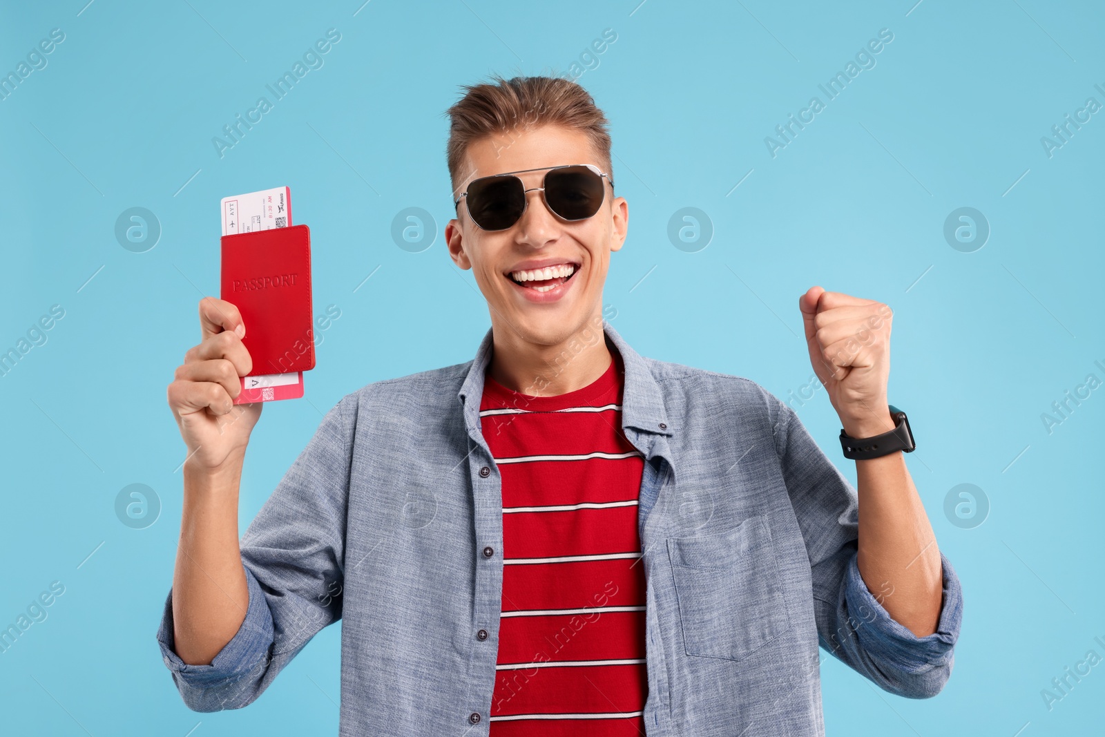 Photo of Happy traveller in sunglasses with passport and ticket on light blue background