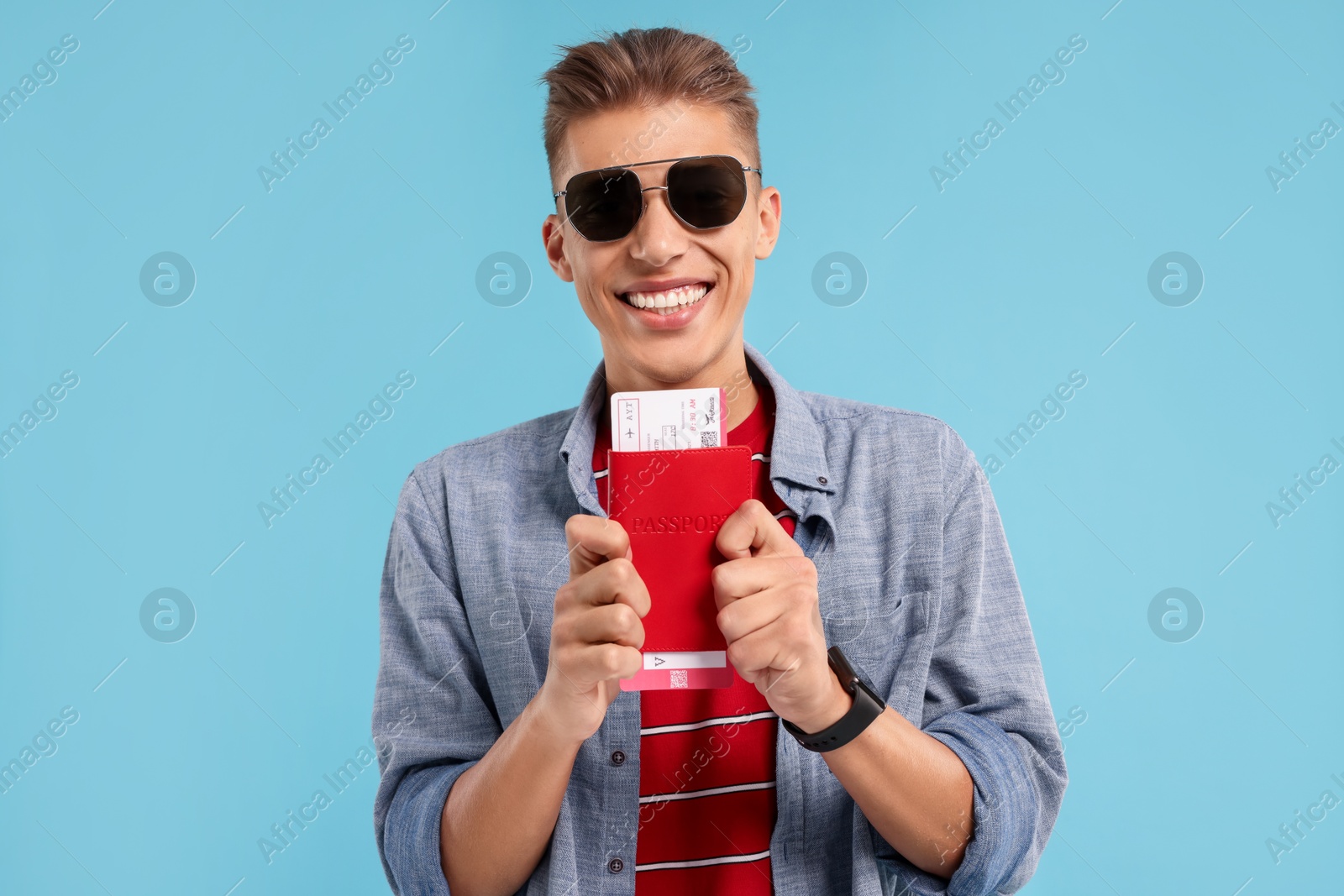 Photo of Happy traveller in sunglasses with passport and ticket on light blue background