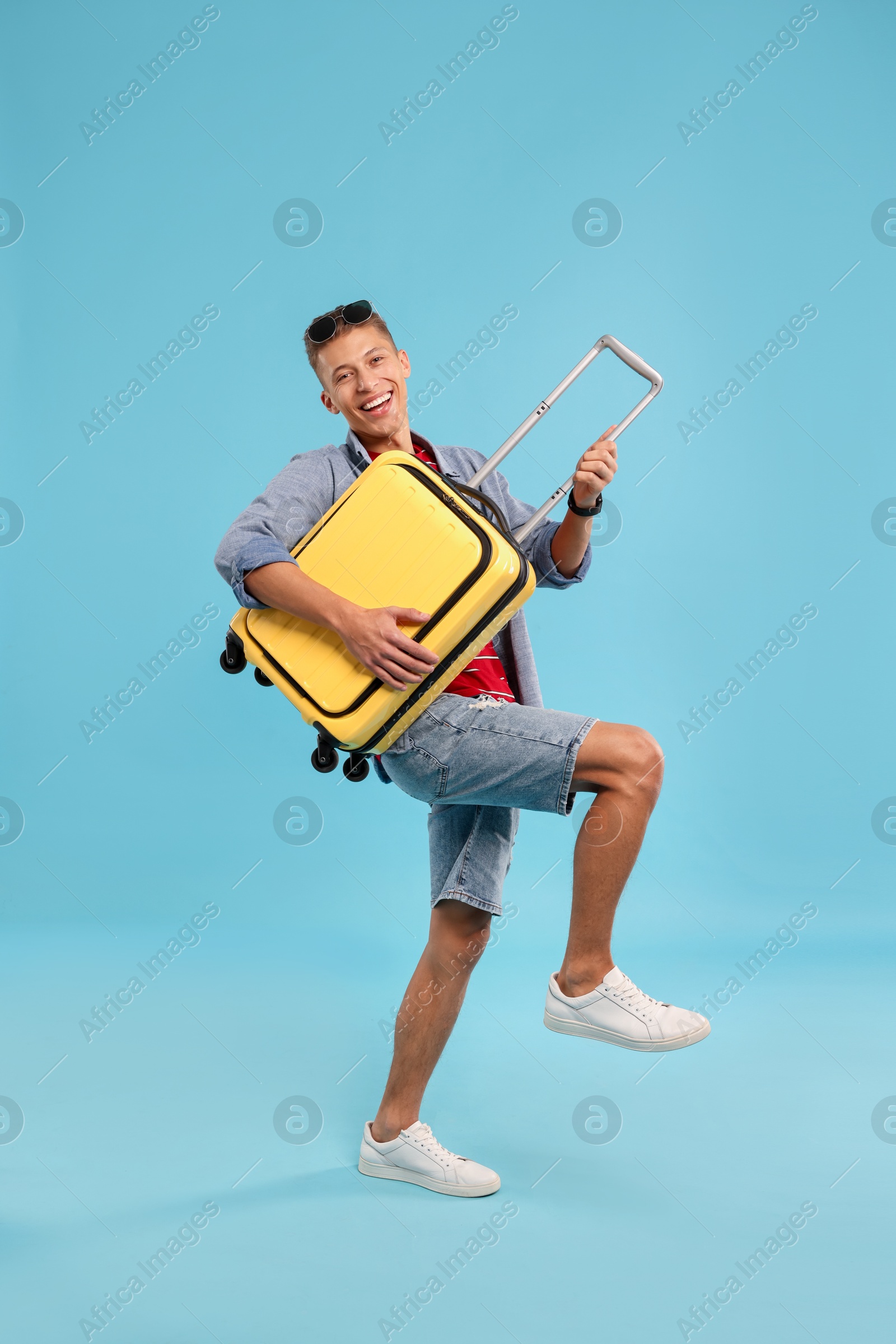 Photo of Happy traveller with suitcase on light blue background