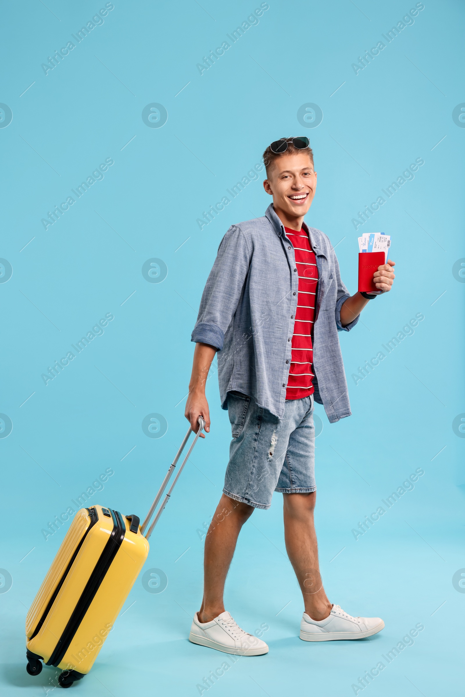 Photo of Happy traveller with suitcase, passport and ticket on light blue background