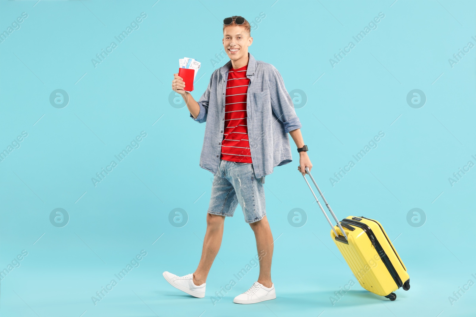 Photo of Happy traveller with suitcase, passport and ticket on light blue background