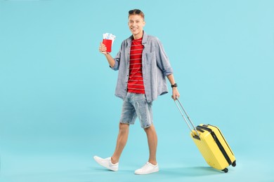 Photo of Happy traveller with suitcase, passport and ticket on light blue background