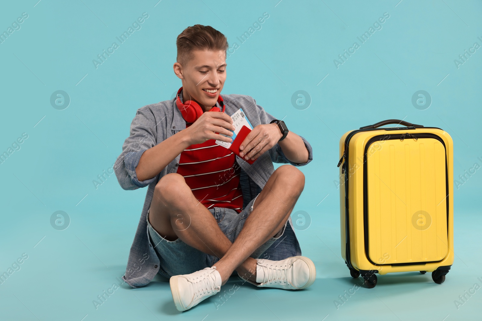 Photo of Happy traveller with suitcase, passport and ticket on light blue background