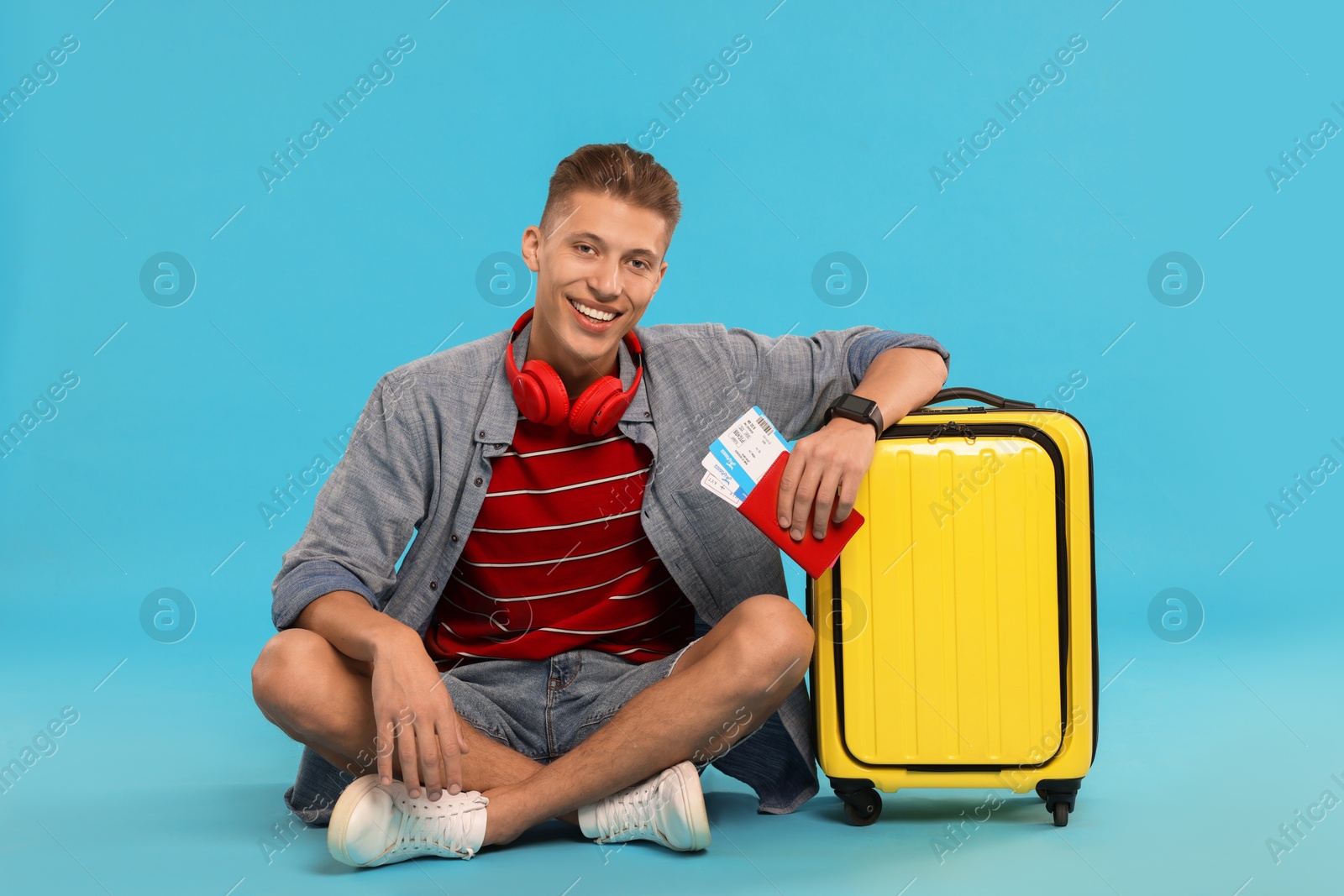 Photo of Happy traveller with suitcase, passport and tickets on light blue background