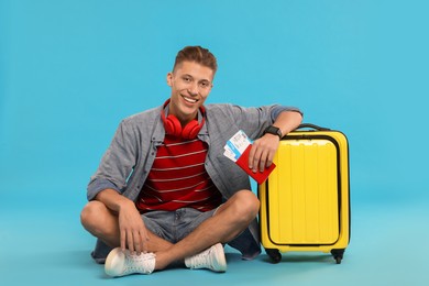 Photo of Happy traveller with suitcase, passport and tickets on light blue background