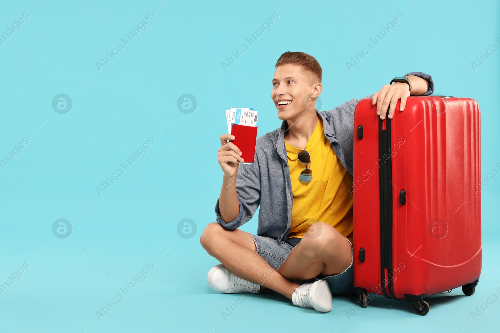 Photo of Happy traveller with suitcase, passport and tickets on light blue background, space for text