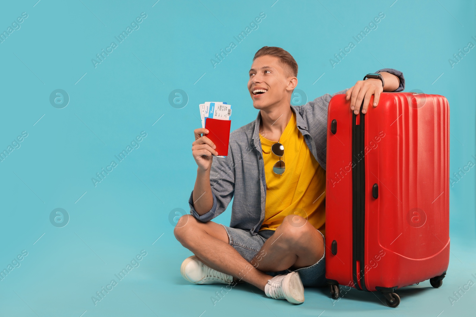 Photo of Happy traveller with suitcase, passport and tickets on light blue background, space for text