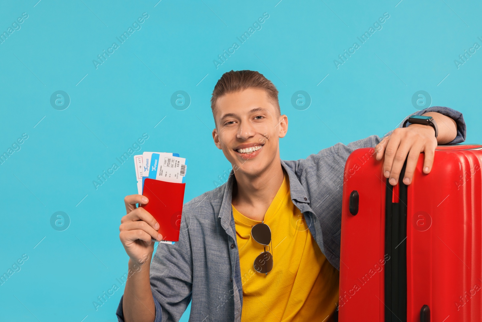 Photo of Happy traveller with suitcase, passport and tickets on light blue background