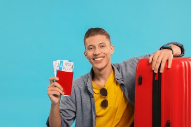 Photo of Happy traveller with suitcase, passport and tickets on light blue background