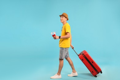 Photo of Happy traveller with suitcase, passport and tickets on light blue background