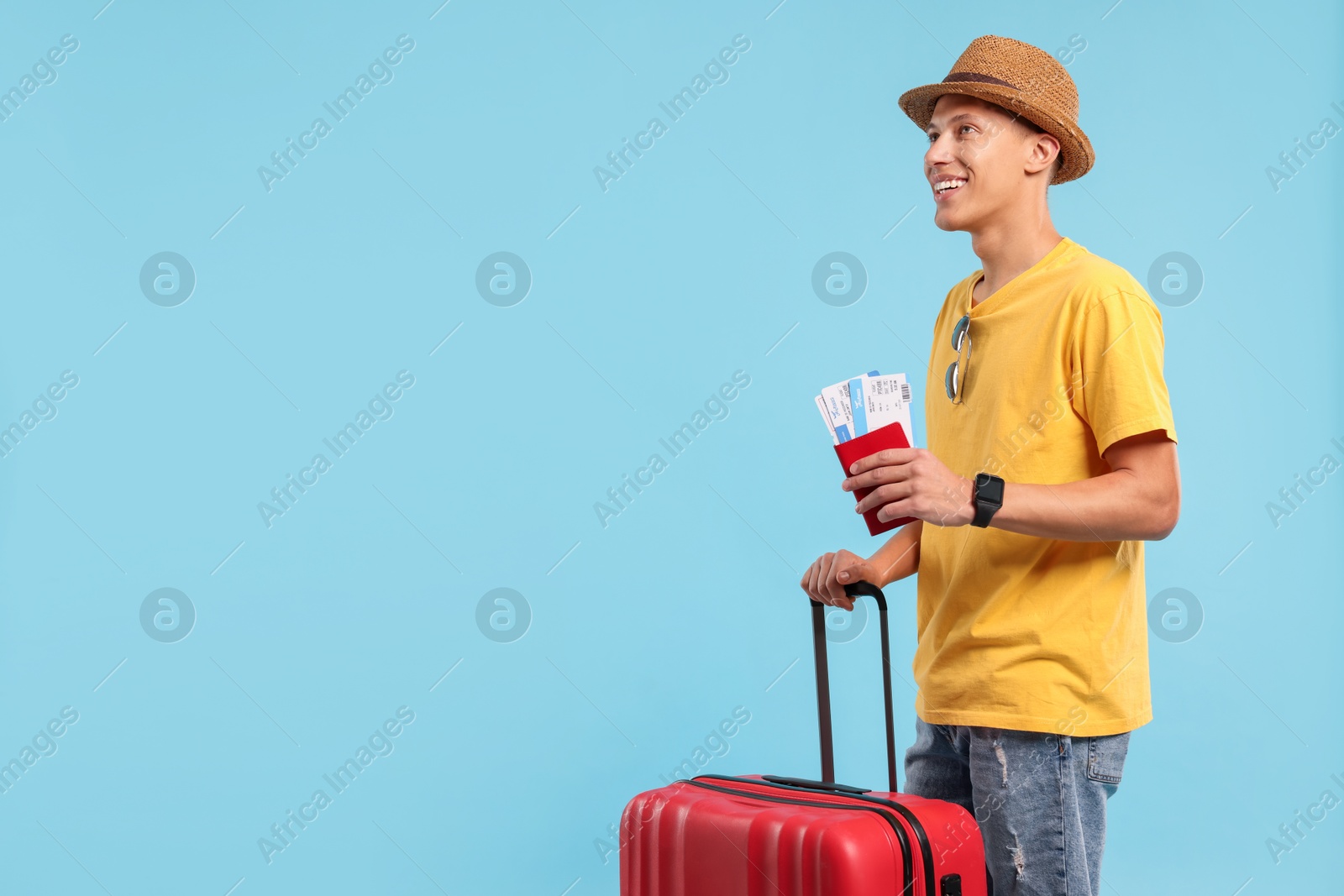 Photo of Happy traveller with suitcase, passport and tickets on light blue background, space for text