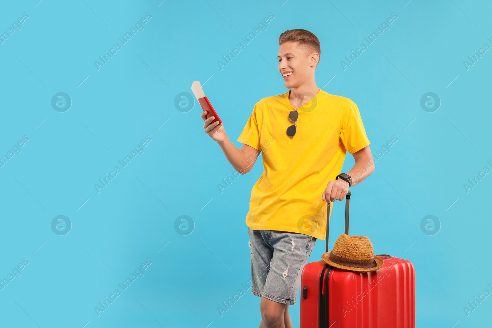 Photo of Happy traveller with suitcase, passport and tickets on light blue background, space for text