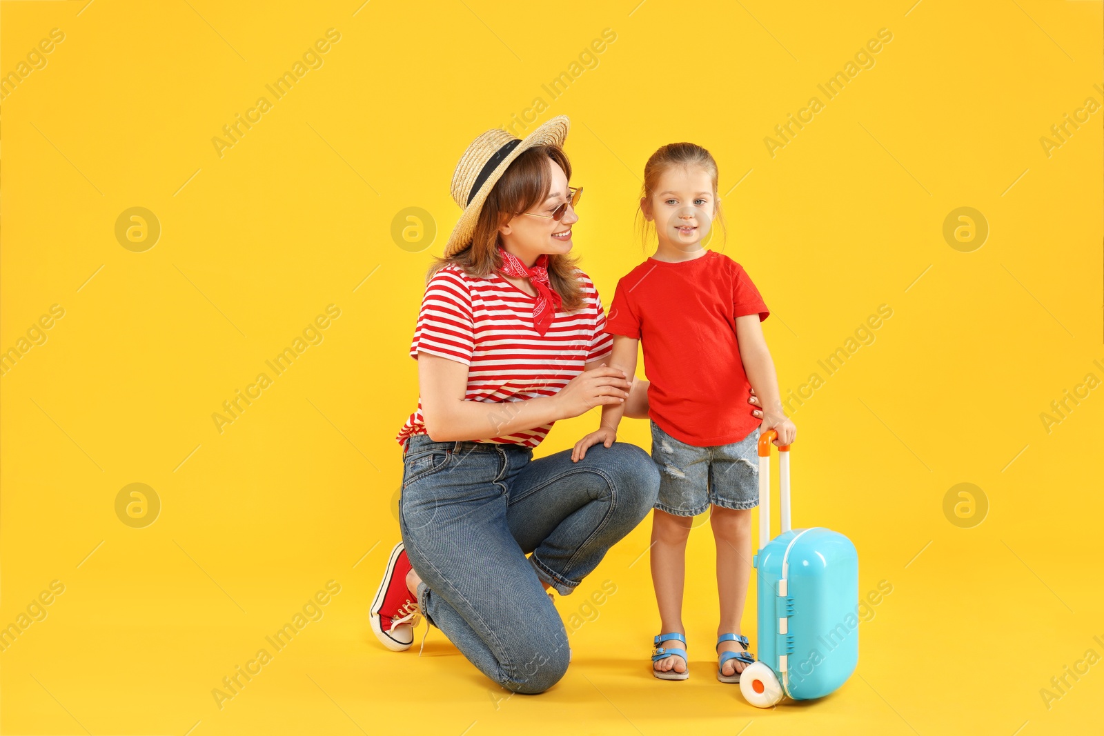 Photo of Traveller with suitcase. Young woman and cute little girl on yellow background