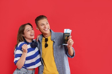 Photo of Happy travellers with passport and tickets on red background, space for text