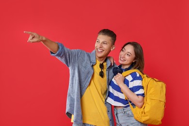 Photo of Traveller with backpack. Happy woman and man pointing at something on red background