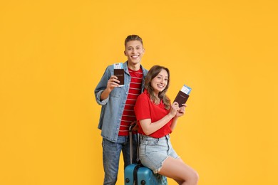 Photo of Happy travellers with suitcase, passports and tickets on yellow background