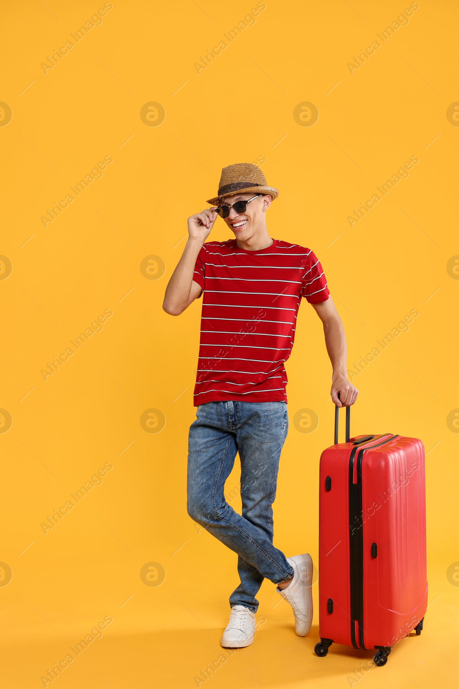 Photo of Happy traveller in sunglasses with suitcase on yellow background