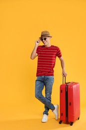 Photo of Happy traveller in sunglasses with suitcase on yellow background