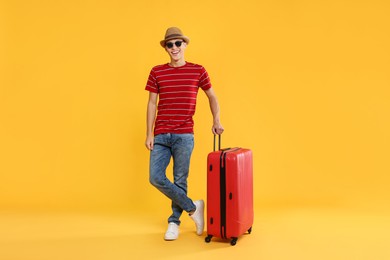 Photo of Happy traveller in sunglasses with suitcase on yellow background