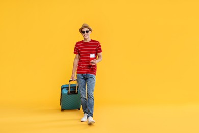 Photo of Happy traveller with suitcase, passport and ticket on yellow background. Space for text