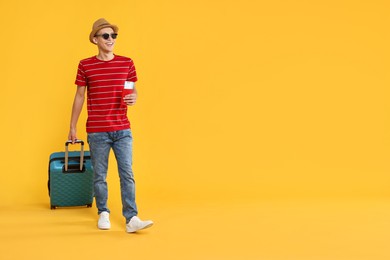 Happy traveller with suitcase, passport and ticket on yellow background, space for text