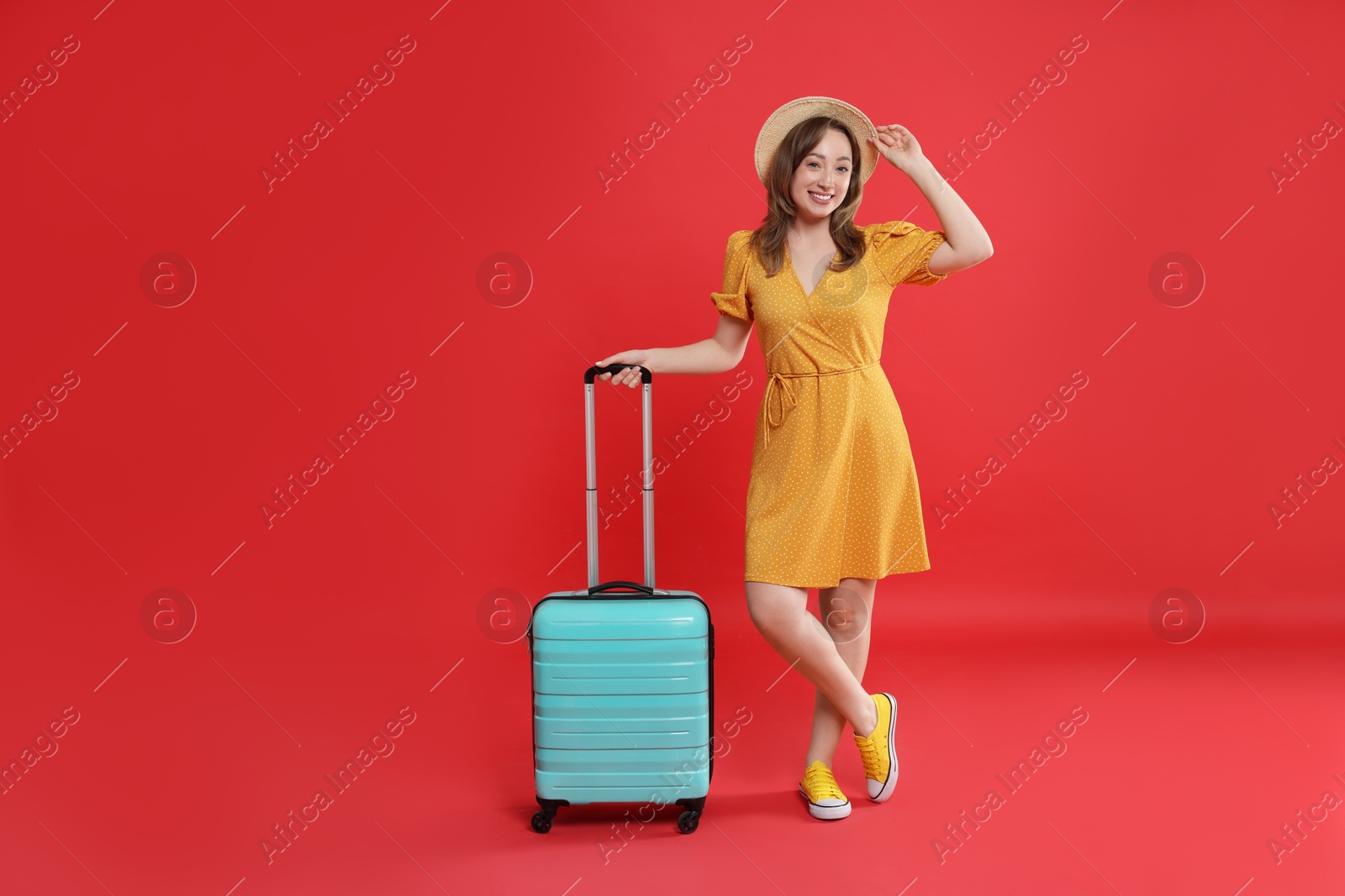 Photo of Happy traveller with suitcase on red background