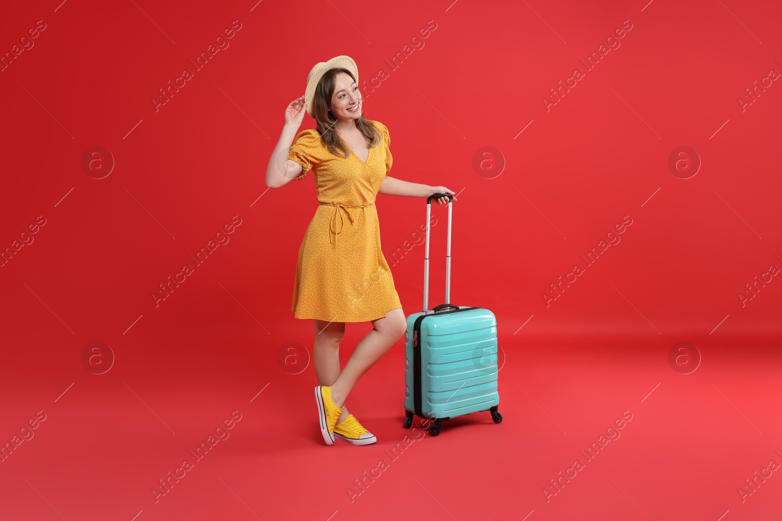 Photo of Happy traveller with suitcase on red background