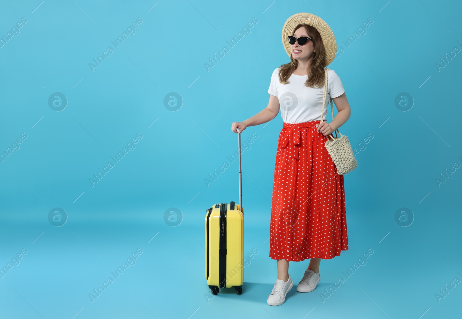 Photo of Happy traveller in sunglasses with suitcase on light blue background, space for text