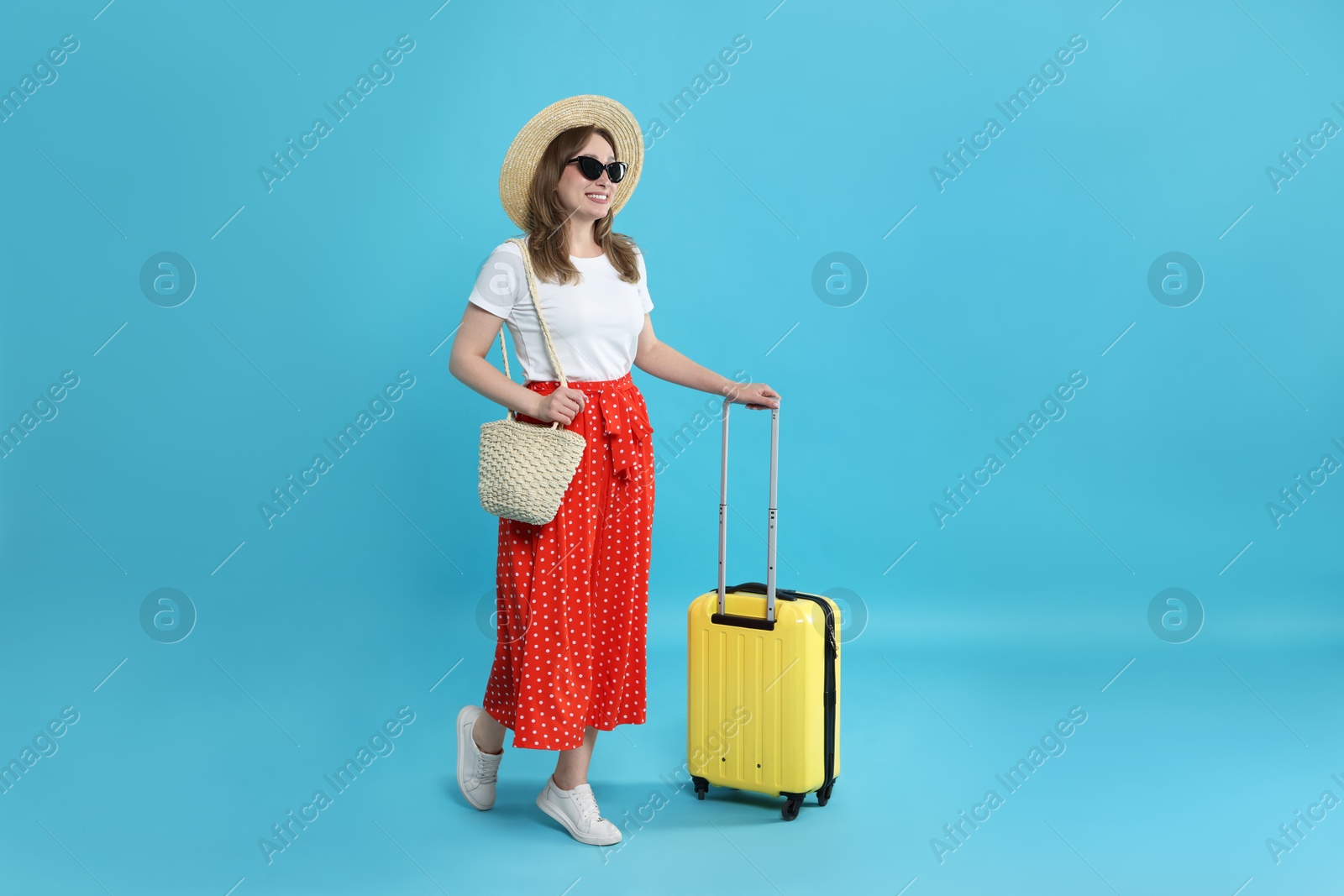 Photo of Happy traveller in sunglasses with suitcase on light blue background