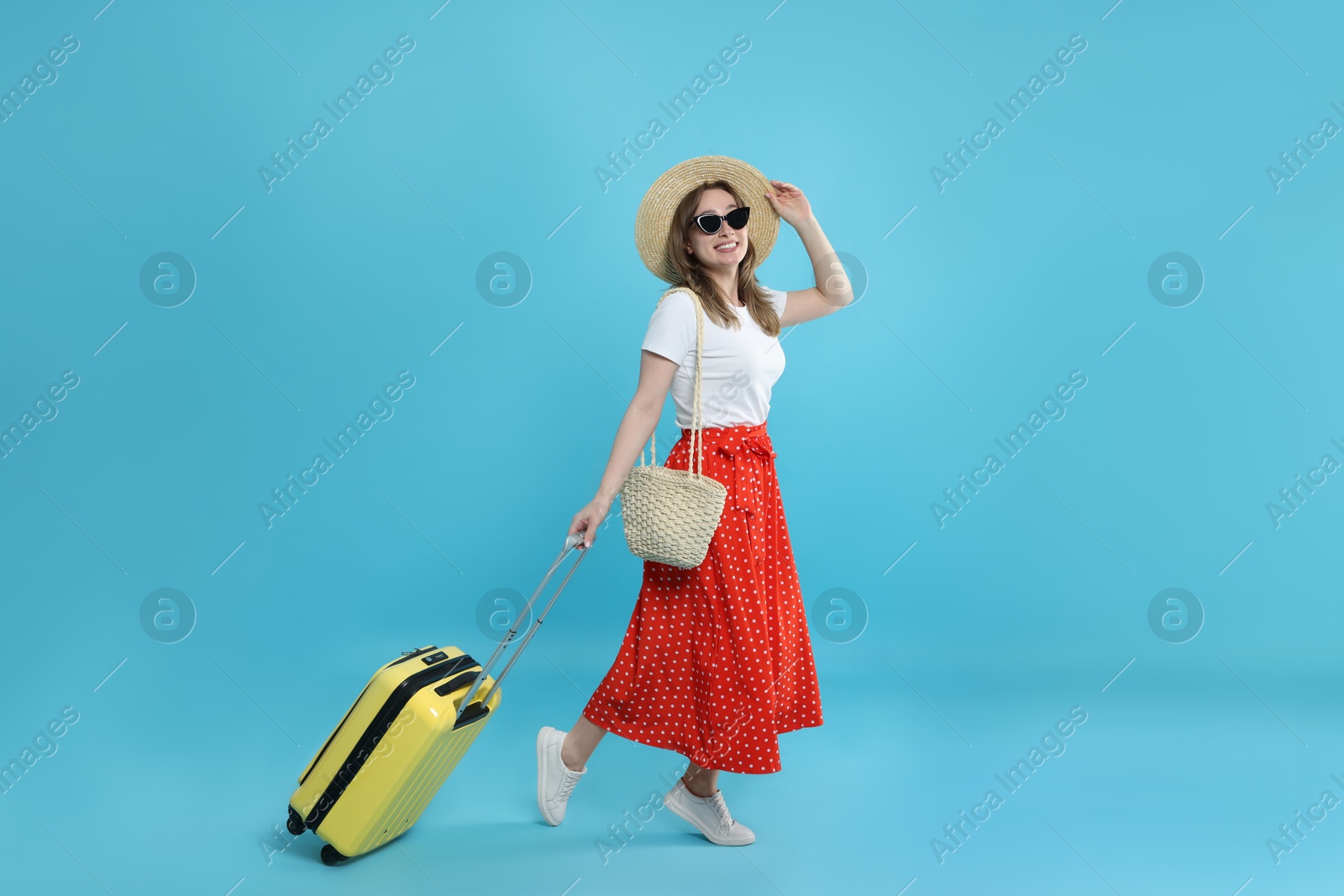 Photo of Happy traveller in sunglasses with suitcase on light blue background