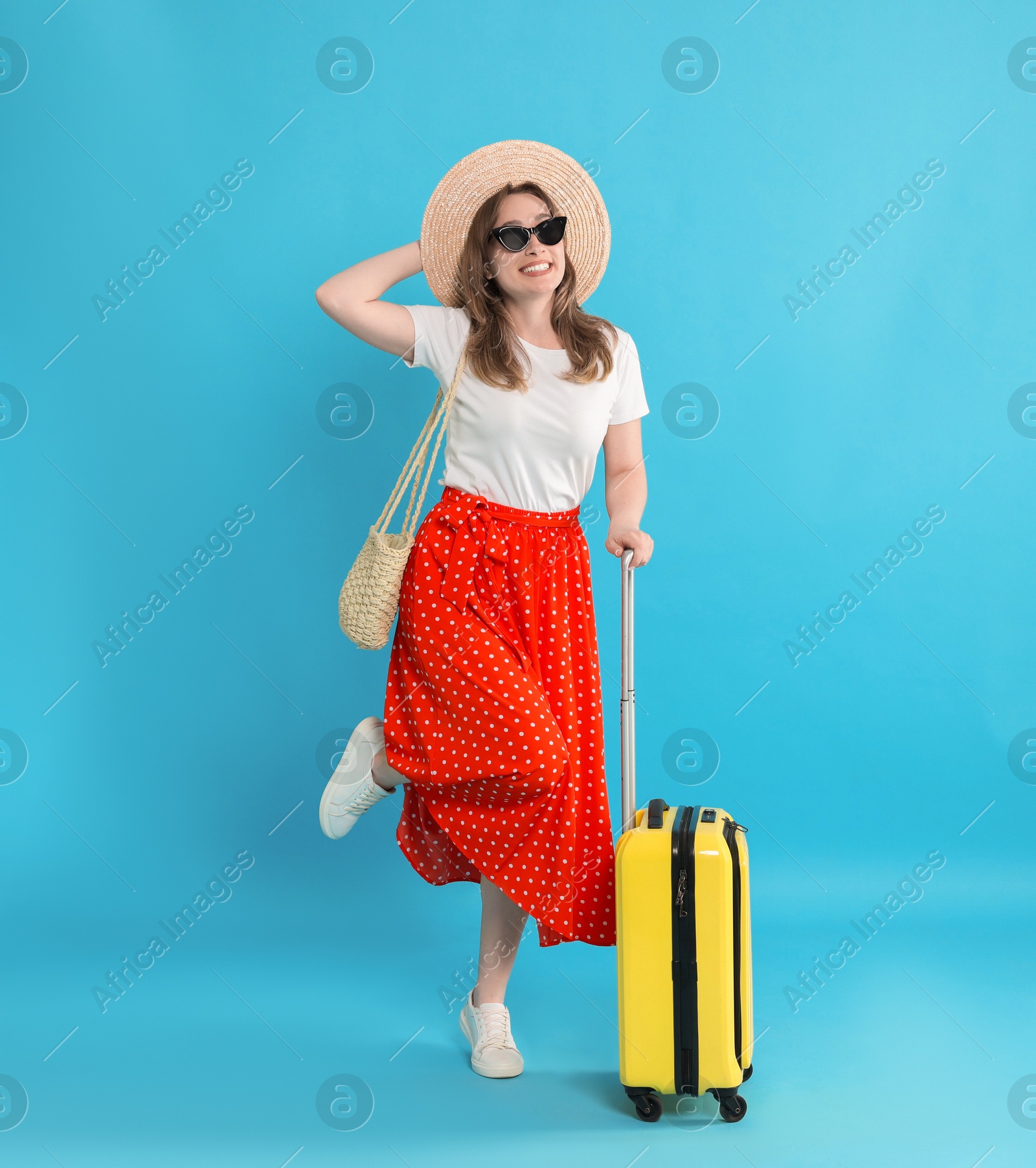 Photo of Happy traveller in sunglasses with suitcase on light blue background