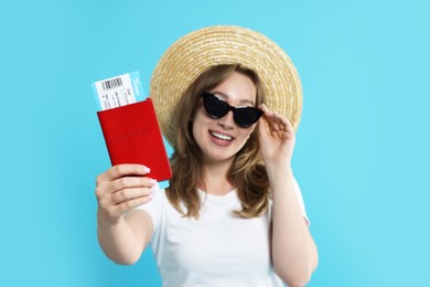 Photo of Happy traveller in sunglasses with passport and ticket on light blue background, selective focus