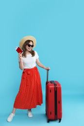 Photo of Happy traveller in sunglasses with suitcase, passport and ticket on light blue background